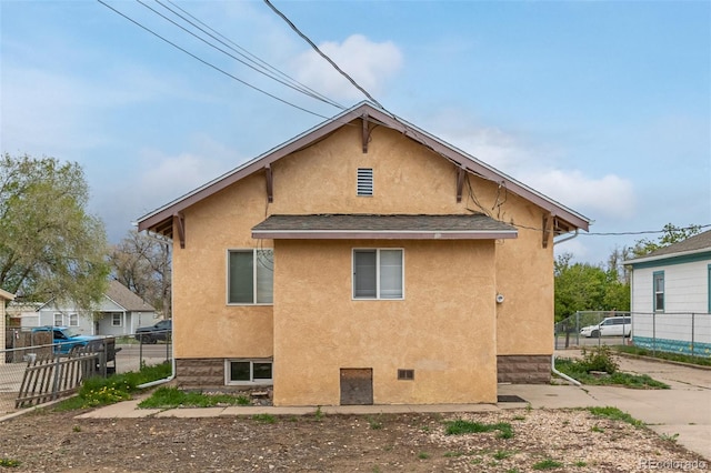 rear view of property with fence, roof with shingles, and stucco siding