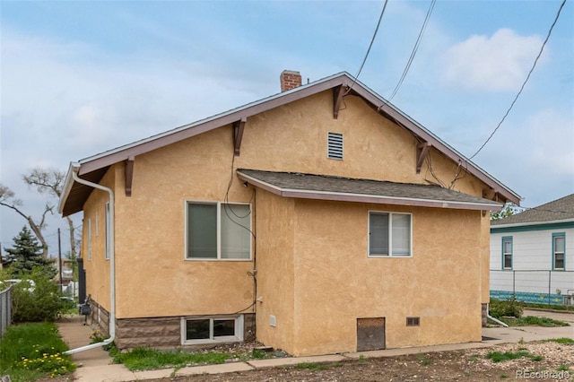 rear view of property featuring fence, stucco siding, a chimney, and roof with shingles