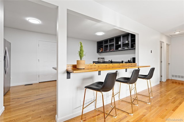 kitchen featuring a breakfast bar, open shelves, wooden counters, freestanding refrigerator, and a peninsula