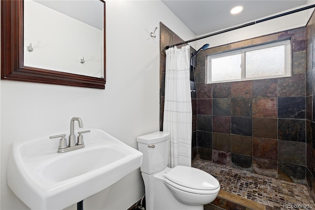 bathroom featuring toilet, a tile shower, and a sink