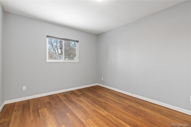 empty room with wood finished floors, visible vents, and baseboards