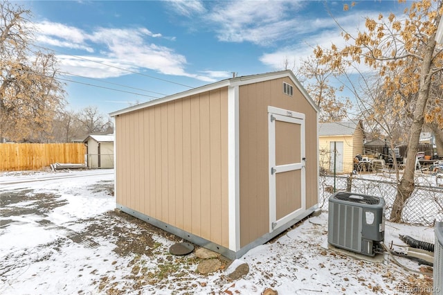 snow covered structure featuring fence, a storage unit, an outdoor structure, and central air condition unit