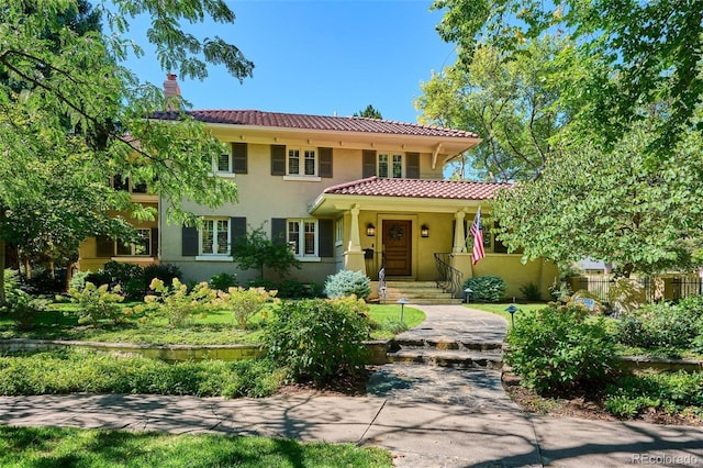 mediterranean / spanish house with a tiled roof, a chimney, and stucco siding