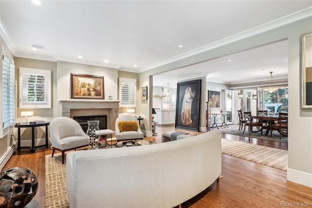 living area featuring crown molding, recessed lighting, a glass covered fireplace, wood finished floors, and baseboards