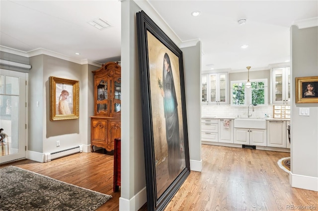 interior space with a baseboard radiator, light wood-style flooring, a sink, baseboards, and crown molding