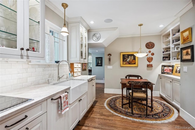 kitchen featuring light stone counters, a sink, white cabinetry, glass insert cabinets, and crown molding