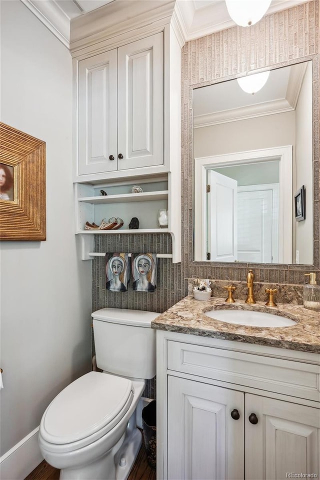 half bathroom with baseboards, vanity, toilet, and crown molding