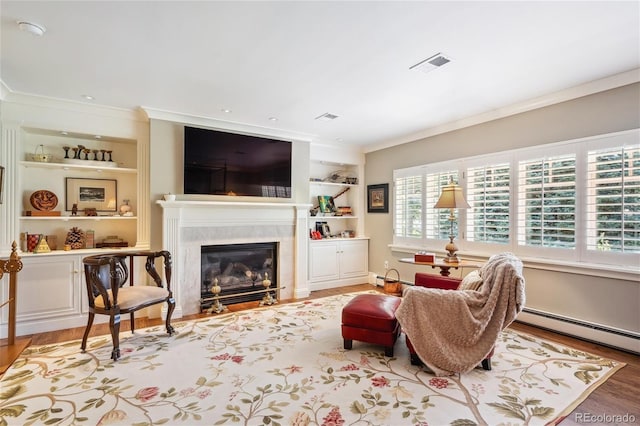 living area featuring built in shelves, crown molding, visible vents, a premium fireplace, and wood finished floors