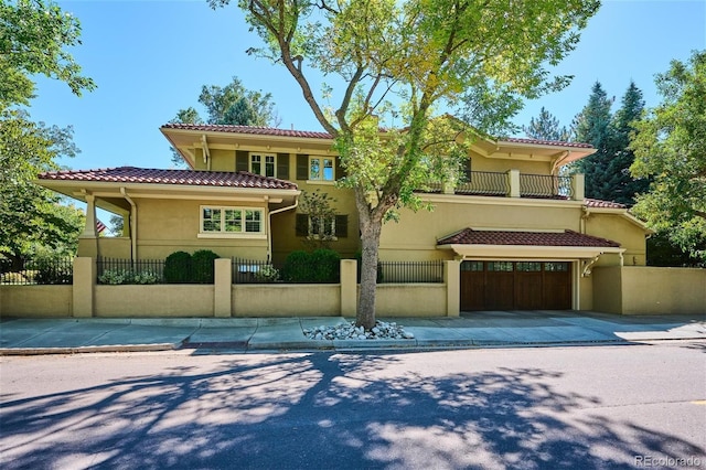 mediterranean / spanish-style house featuring a fenced front yard, a balcony, a tiled roof, concrete driveway, and stucco siding