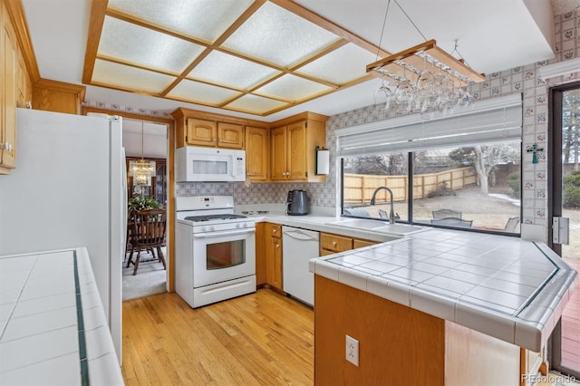 kitchen featuring tile countertops, a peninsula, white appliances, a sink, and brown cabinets