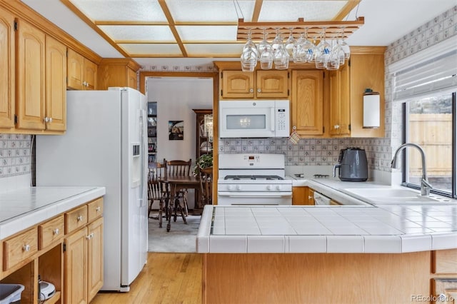 kitchen featuring tasteful backsplash, light wood-style floors, a sink, white appliances, and a peninsula