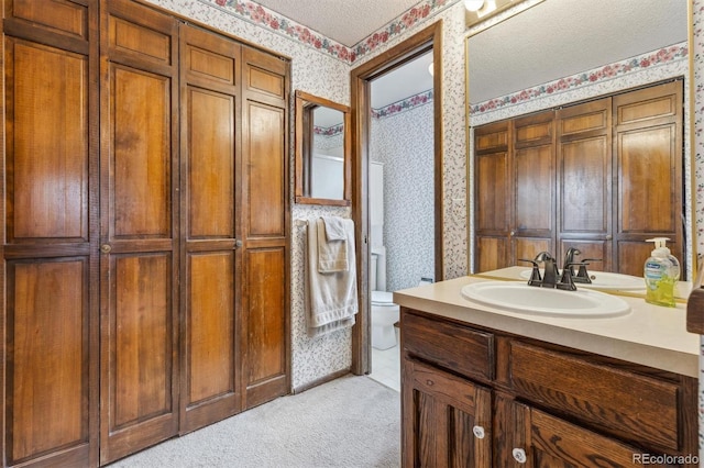 full bathroom with wallpapered walls, toilet, a textured ceiling, vanity, and a closet