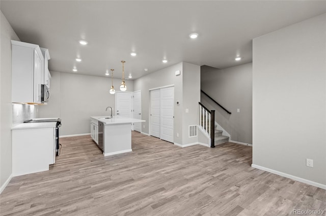 kitchen with stainless steel microwave, light countertops, light wood-style floors, white cabinetry, and a sink