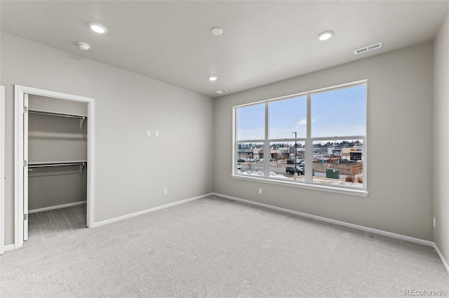 unfurnished bedroom with visible vents, a walk in closet, recessed lighting, carpet, and baseboards