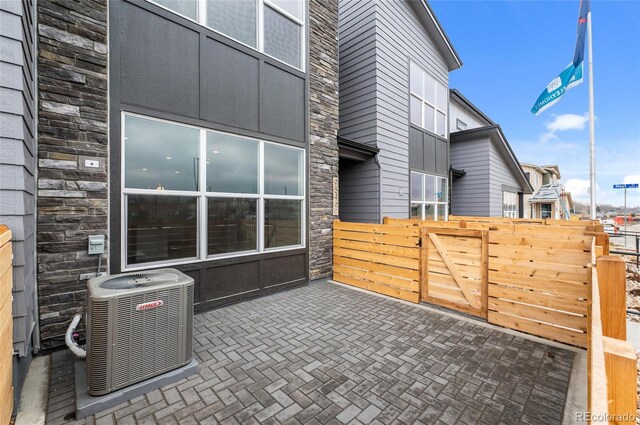 exterior space featuring a patio, central air condition unit, fence, and stone siding