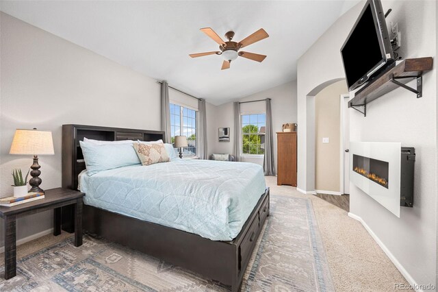 4467 Trailside Ln, Castle Rock, CO 80109 - bedroom featuring a lit fireplace, baseboards, light carpet, lofted ceiling, and arched walkways