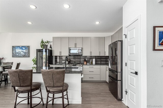 kitchen featuring appliances with stainless steel finishes, gray cabinets, dark wood-style floors, tasteful backsplash, and a kitchen bar