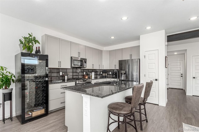 kitchen featuring appliances with stainless steel finishes, a sink, gray cabinets, light wood-style floors, and dark stone counters