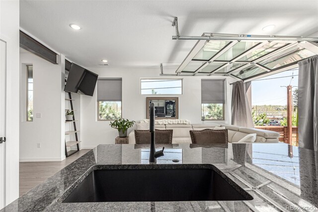 kitchen with a sink, wood finished floors, dark stone countertops, recessed lighting, and baseboards