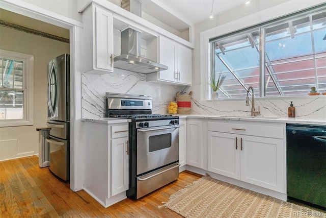 kitchen featuring white cabinetry, appliances with stainless steel finishes, light wood-type flooring, wall chimney exhaust hood, and sink