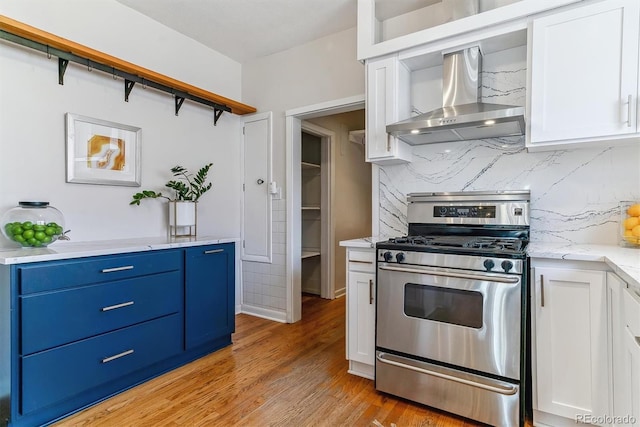 kitchen featuring light hardwood / wood-style floors, stainless steel range with gas cooktop, backsplash, wall chimney exhaust hood, and white cabinets