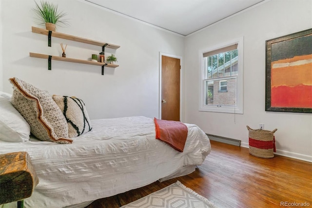 bedroom with a baseboard heating unit, ornamental molding, and wood-type flooring