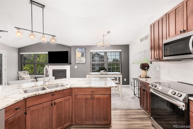 2955 Blue Sky Cir Unit 6-307, Erie, CO 80516 - kitchen with appliances with stainless steel finishes, vaulted ceiling, light wood finished floors, a glass covered fireplace, and a chandelier