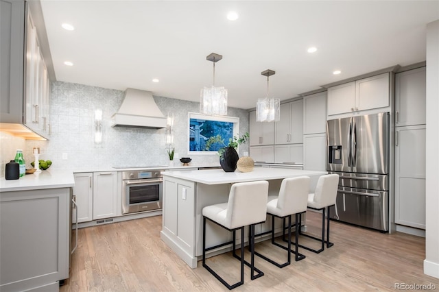 kitchen with stainless steel appliances, a kitchen island, light countertops, gray cabinets, and custom range hood