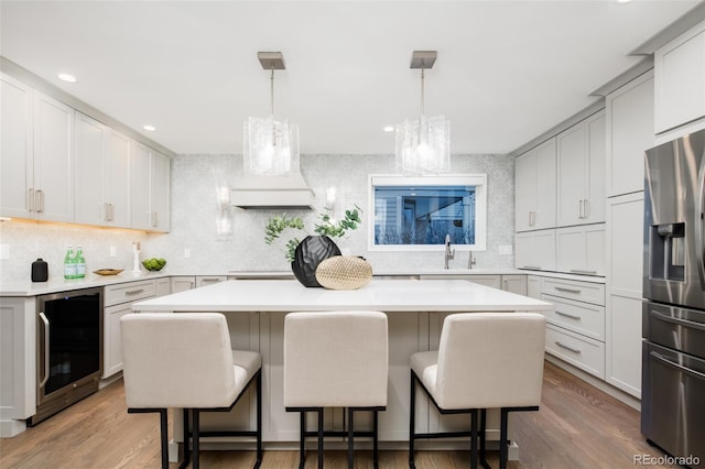 kitchen featuring wine cooler, light countertops, a kitchen island, and stainless steel fridge with ice dispenser