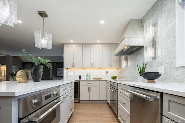 kitchen featuring custom exhaust hood, light countertops, backsplash, appliances with stainless steel finishes, and light wood-style floors