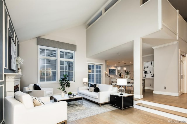 living room featuring baseboards, a fireplace, high vaulted ceiling, and wood finished floors