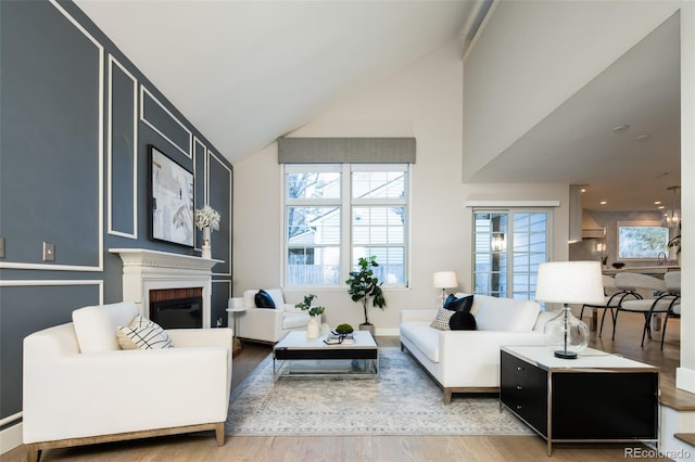 living area with a brick fireplace, high vaulted ceiling, and wood finished floors