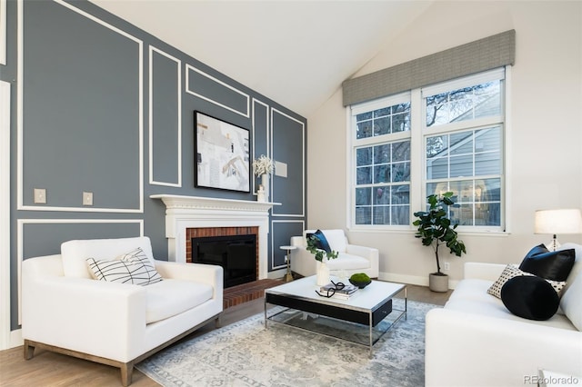 living area with a brick fireplace, vaulted ceiling, and wood finished floors