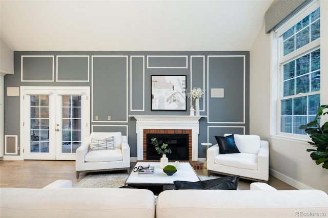 living area featuring french doors, a fireplace, baseboards, and wood finished floors