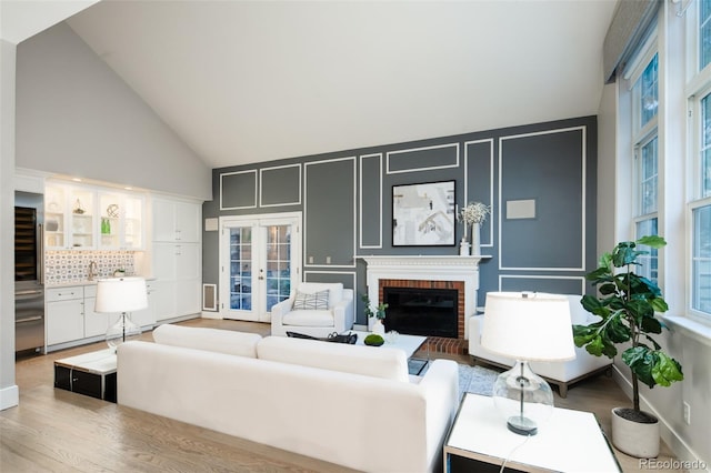 living area featuring a healthy amount of sunlight, a brick fireplace, high vaulted ceiling, and french doors