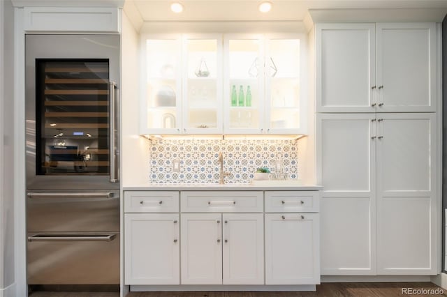 kitchen with wine cooler, light countertops, backsplash, white cabinetry, and a sink