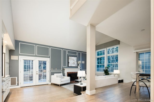 living room featuring light wood-type flooring, a brick fireplace, french doors, and a high ceiling