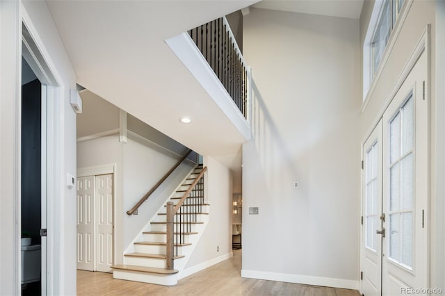 foyer with stairs, a high ceiling, baseboards, and wood finished floors