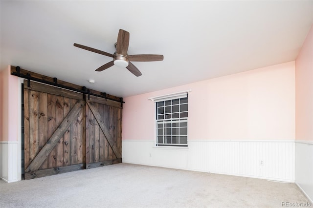 carpeted spare room with a ceiling fan, a wainscoted wall, and a barn door