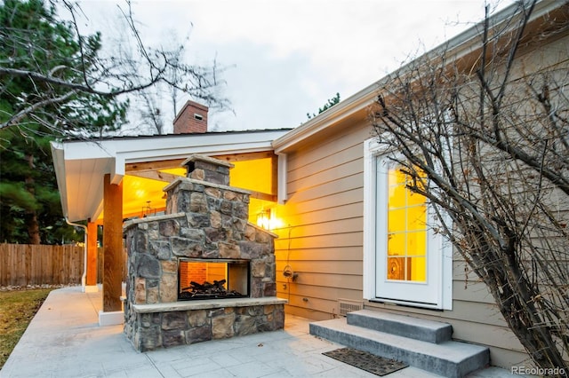 doorway to property with a patio area, an outdoor stone fireplace, a chimney, and fence