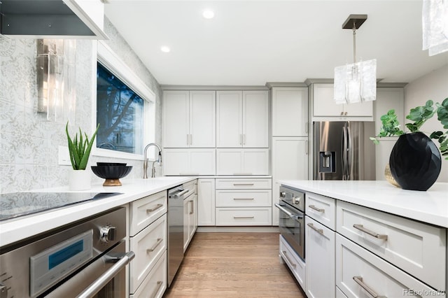 kitchen featuring light countertops, light wood-type flooring, decorative light fixtures, decorative backsplash, and appliances with stainless steel finishes