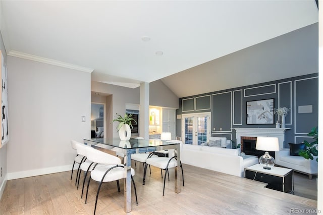 dining space featuring vaulted ceiling, wood finished floors, ornamental molding, baseboards, and a brick fireplace