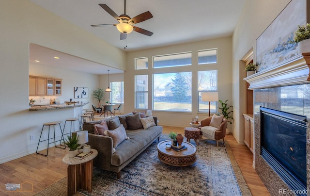 living room featuring a tiled fireplace, ceiling fan, and light hardwood / wood-style flooring