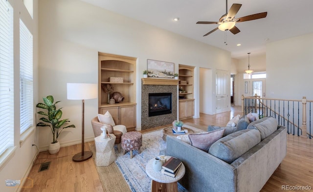 living room featuring built in shelves, ceiling fan, a tile fireplace, and light hardwood / wood-style flooring