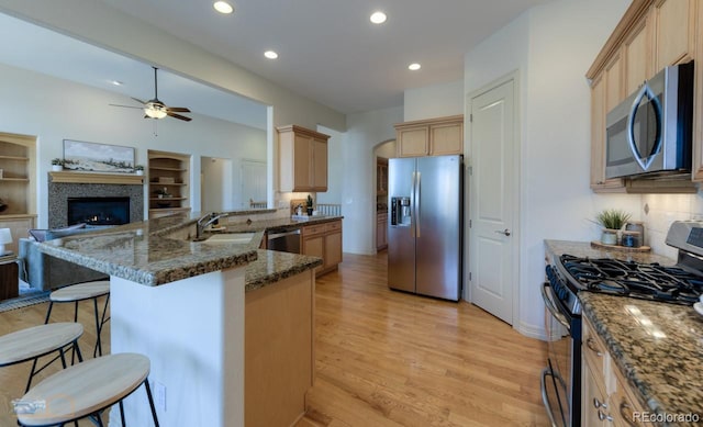 kitchen with light hardwood / wood-style flooring, stainless steel appliances, kitchen peninsula, a kitchen bar, and dark stone counters