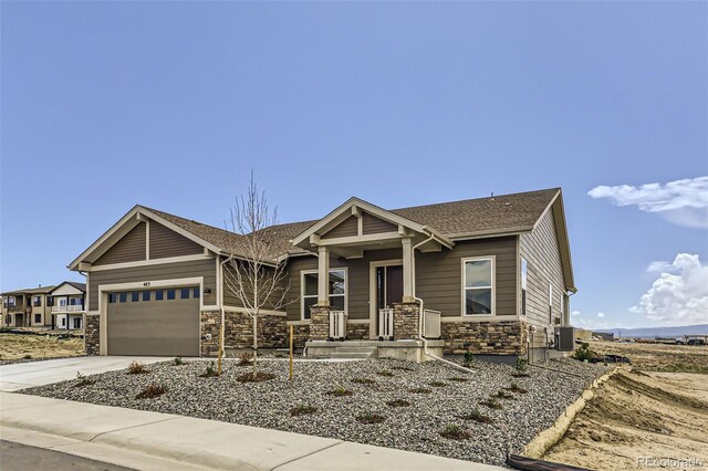view of front facade with stone siding, a garage, concrete driveway, central air condition unit, and a shingled roof