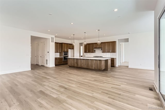 kitchen featuring open floor plan, light countertops, baseboards, light wood finished floors, and a large island with sink