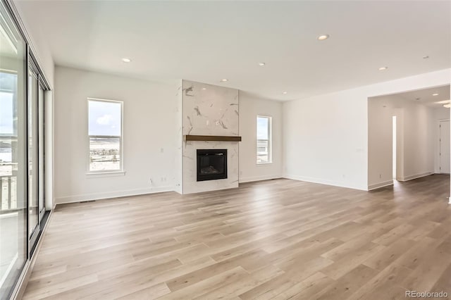 unfurnished living room with light wood-style flooring, a premium fireplace, recessed lighting, and baseboards
