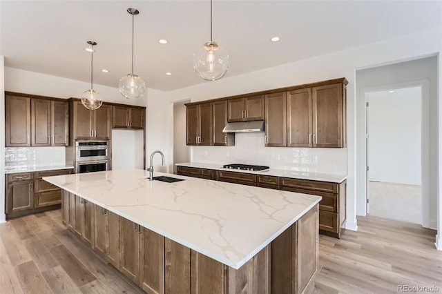 kitchen with a sink, under cabinet range hood, double oven, decorative backsplash, and gas cooktop