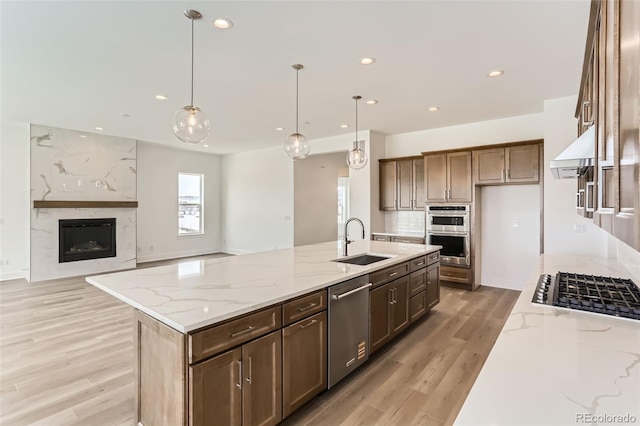 kitchen with a sink, stainless steel appliances, light wood-type flooring, light stone counters, and recessed lighting